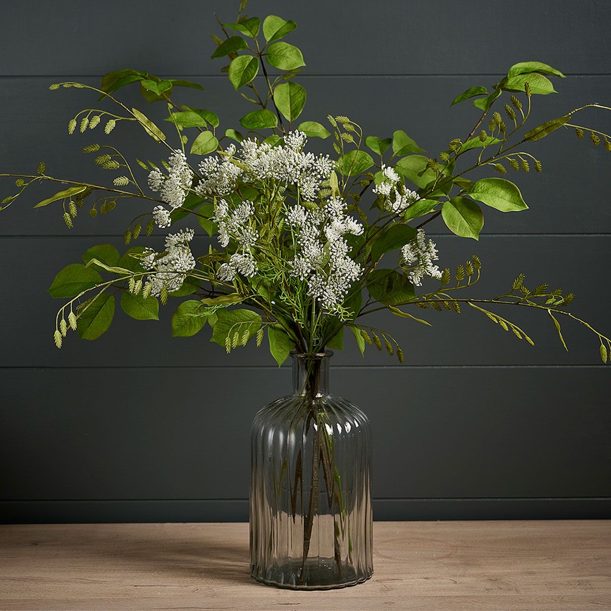 Summer leaves and cow parsley stems arranged in a ribbed glass vase