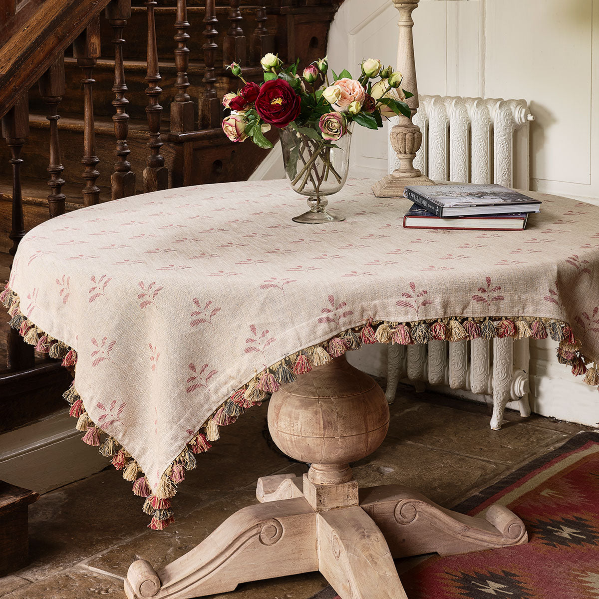 Red Leaf rustic linen tablecloth with tassel trim on a round table with roses