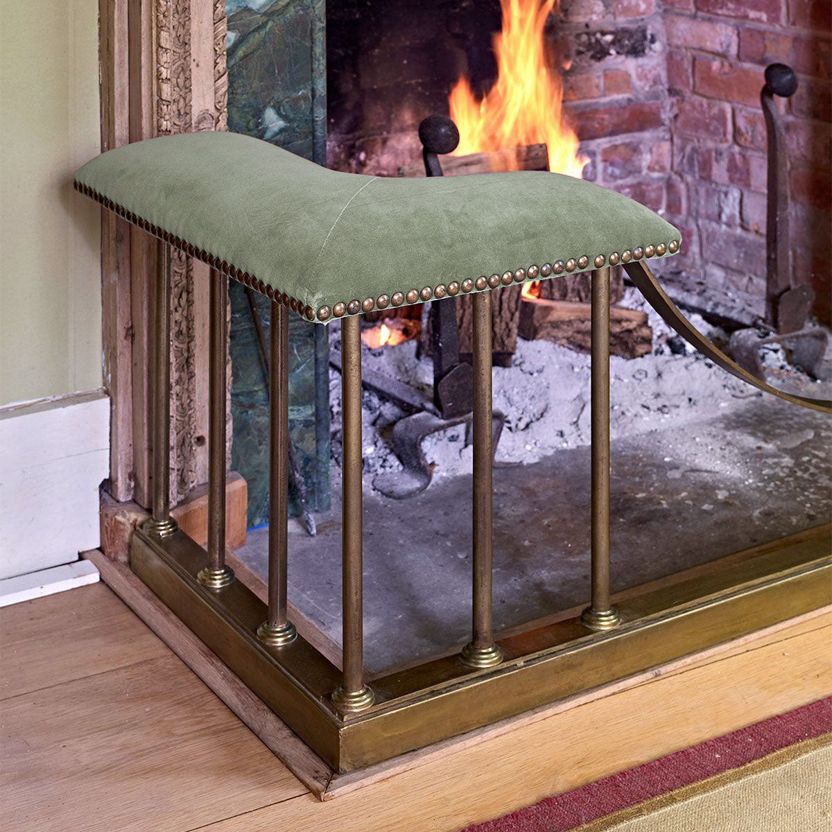 Fire fender upholstered in smokey green velvet at a brick fireplace
